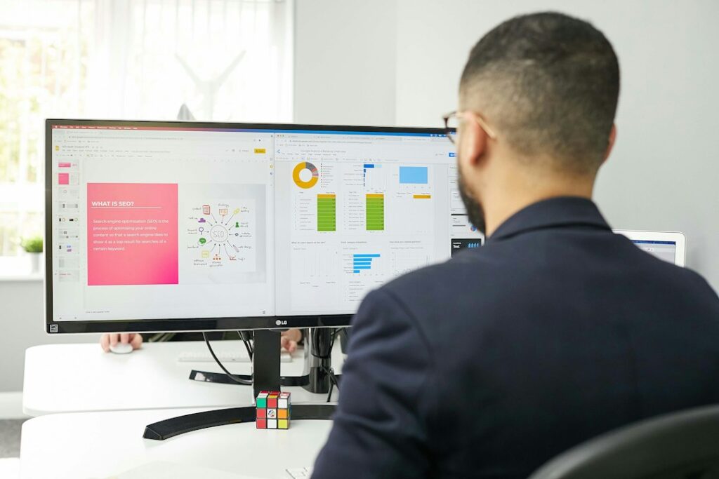 Employee reviews a workflow dashboard beside a laptop, notebook, and organized process documents.