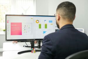 Employee reviews a workflow dashboard beside a laptop, notebook, and organized process documents.